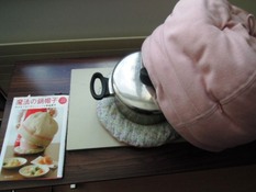 机の上に魔法の鍋帽子の紹介本が置いてあり、本の右隣には魔法の鍋帽子が鍋にかぶさっています。